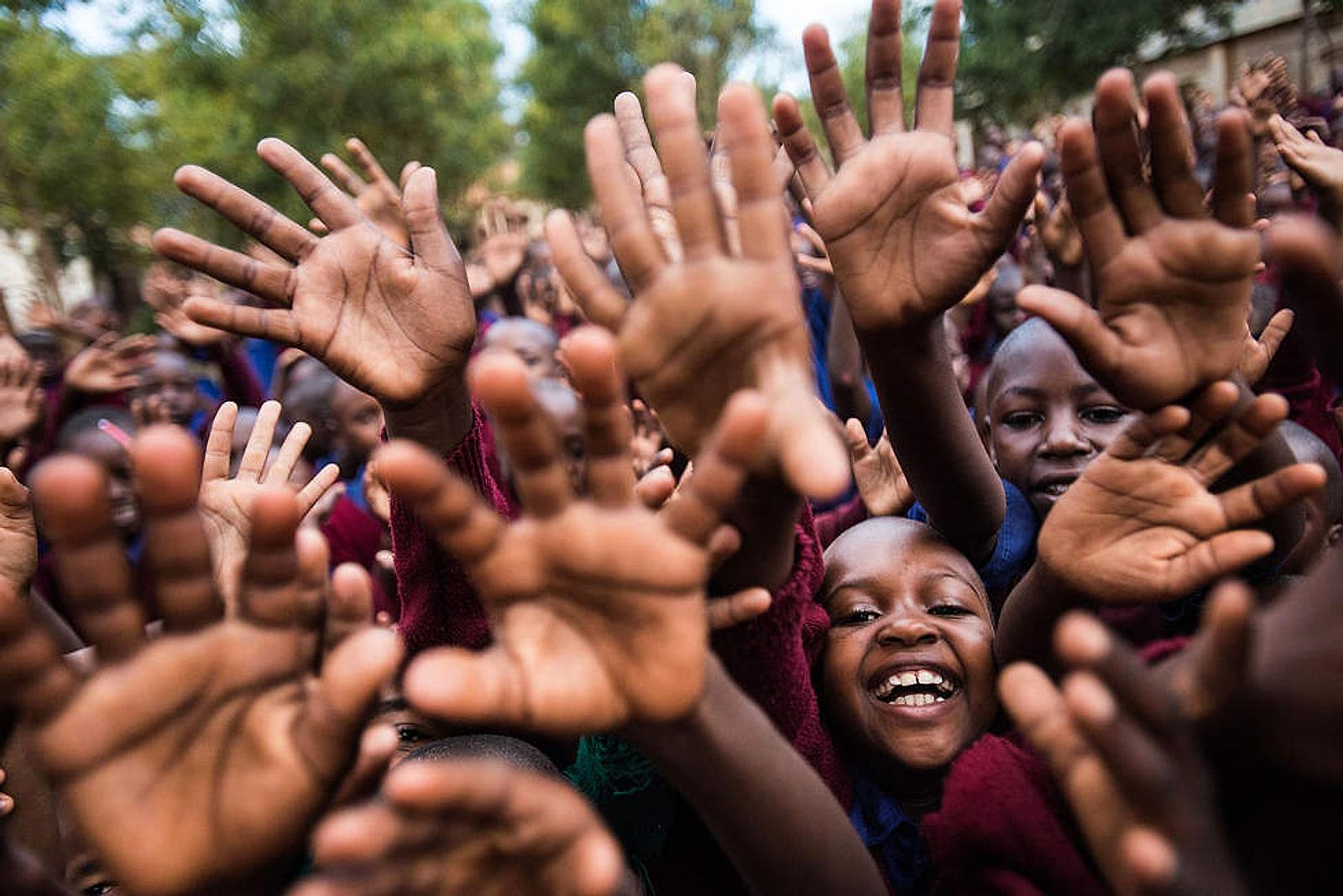 A crowd of schoolchildren raising their open hands towards the camera, one child laughing