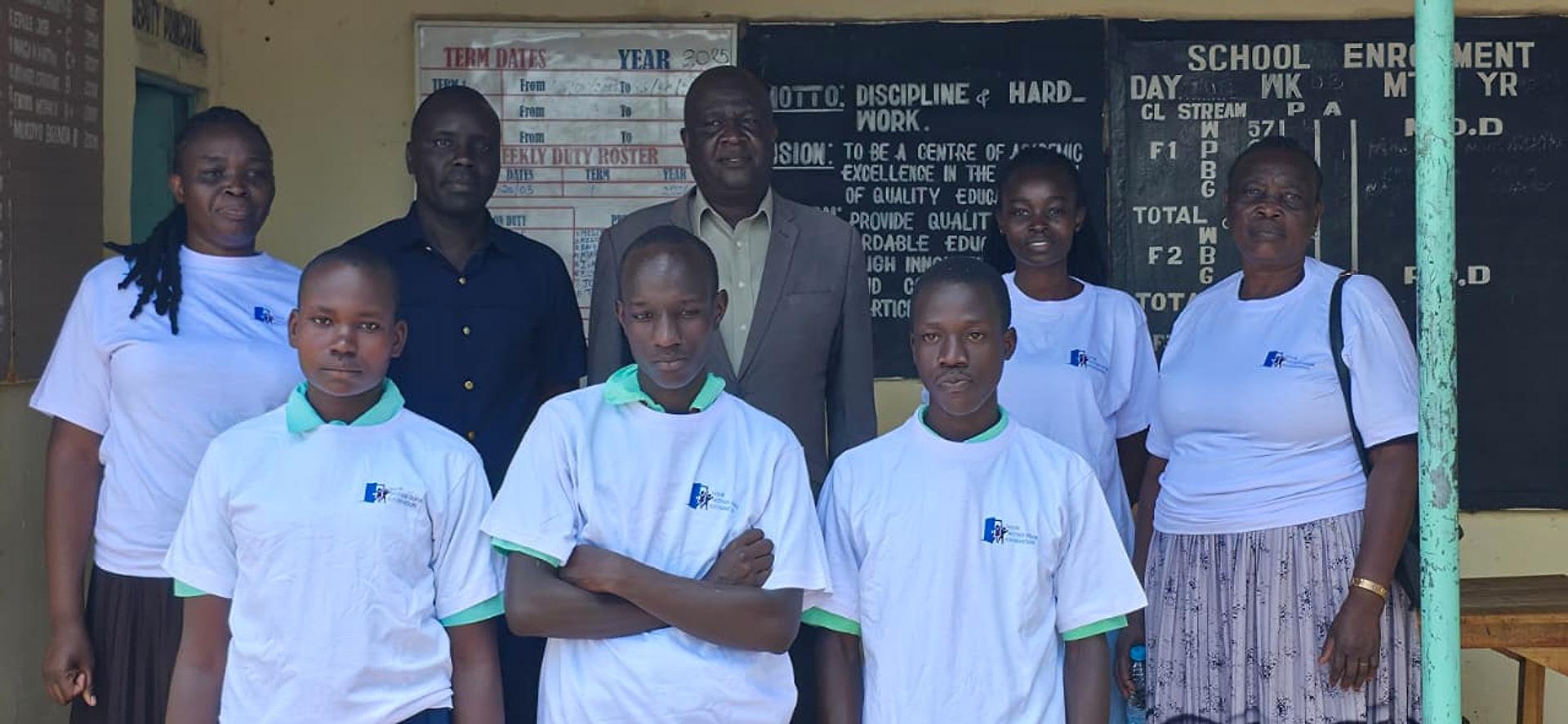 Members of the Door Within Door Foundation community in Foundation t-shirts, standing with students outside a school office