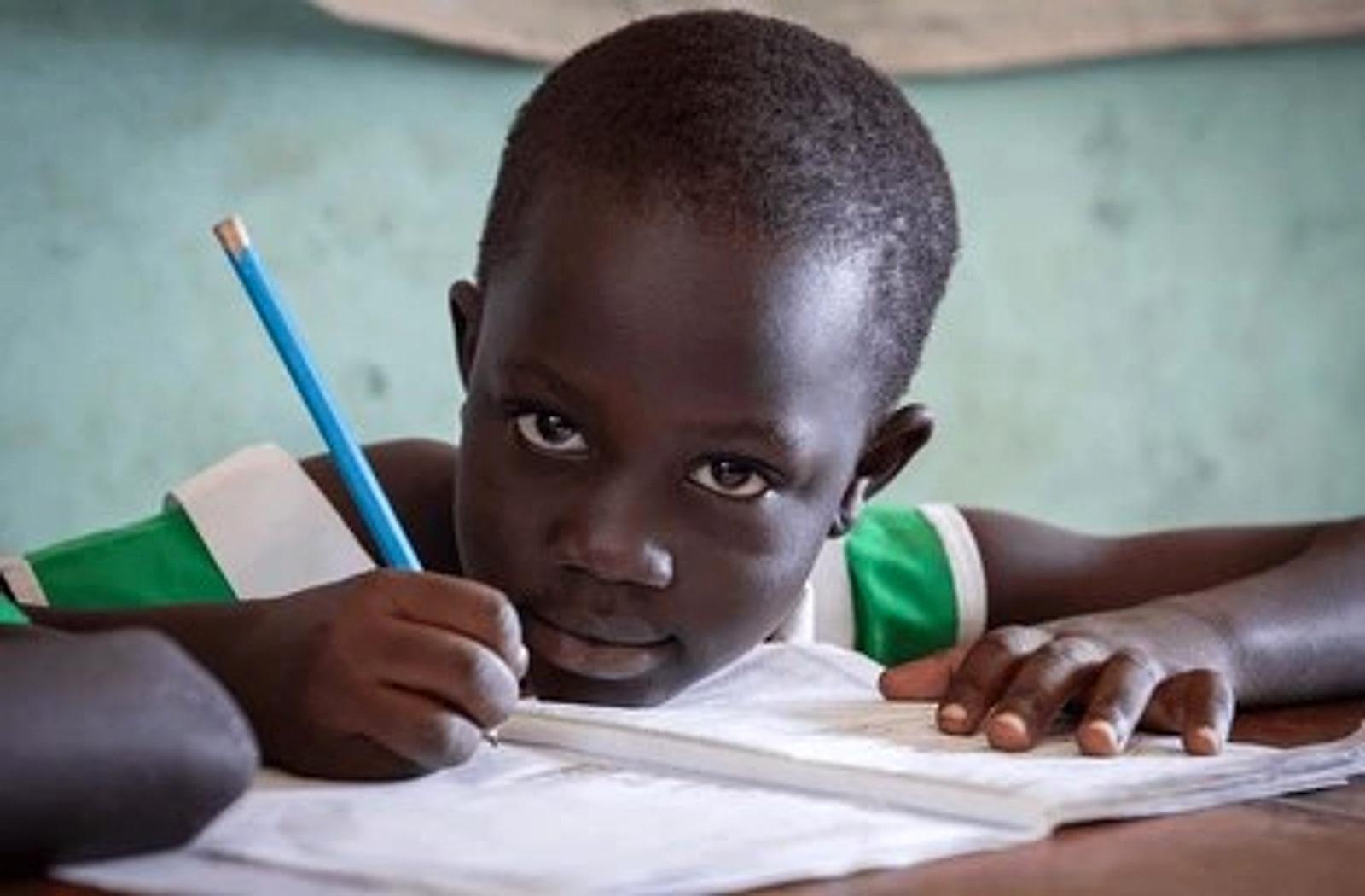 A student writing in an exercise book, looking up at the camera